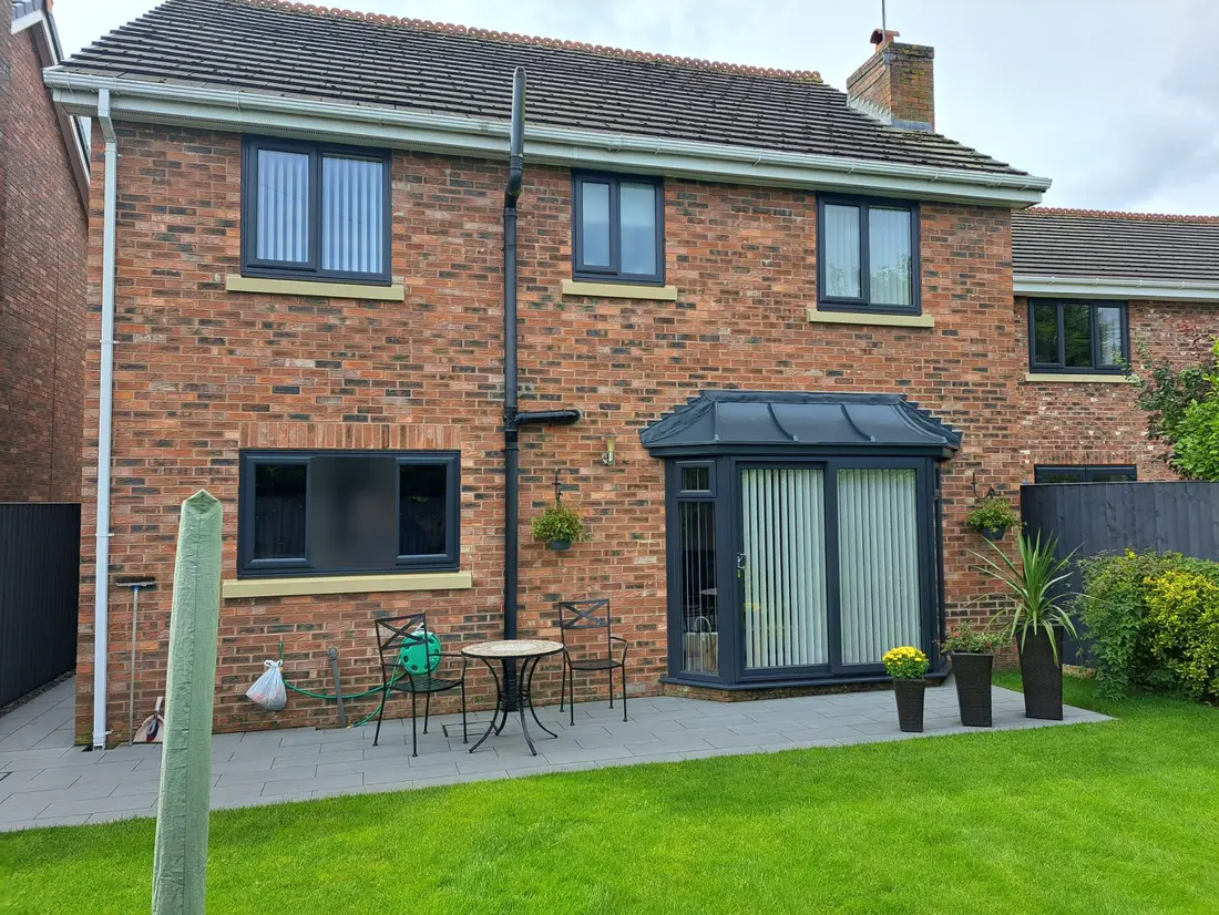 The back of a brick house with new grey windows and a bay